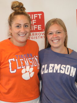 Two Gift of Life Campus Ambassadors post in their Clemson University tee shirts. These two young white ladies have big smiles and look happy to be at the symposium.
