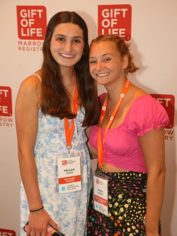 Two female Gift of Life Campus Ambassadors post in front of a Gift of Life backdrop. Both are white, the young lady on the left is brunette, the one on the right is blonde, and both have huge smiles. 